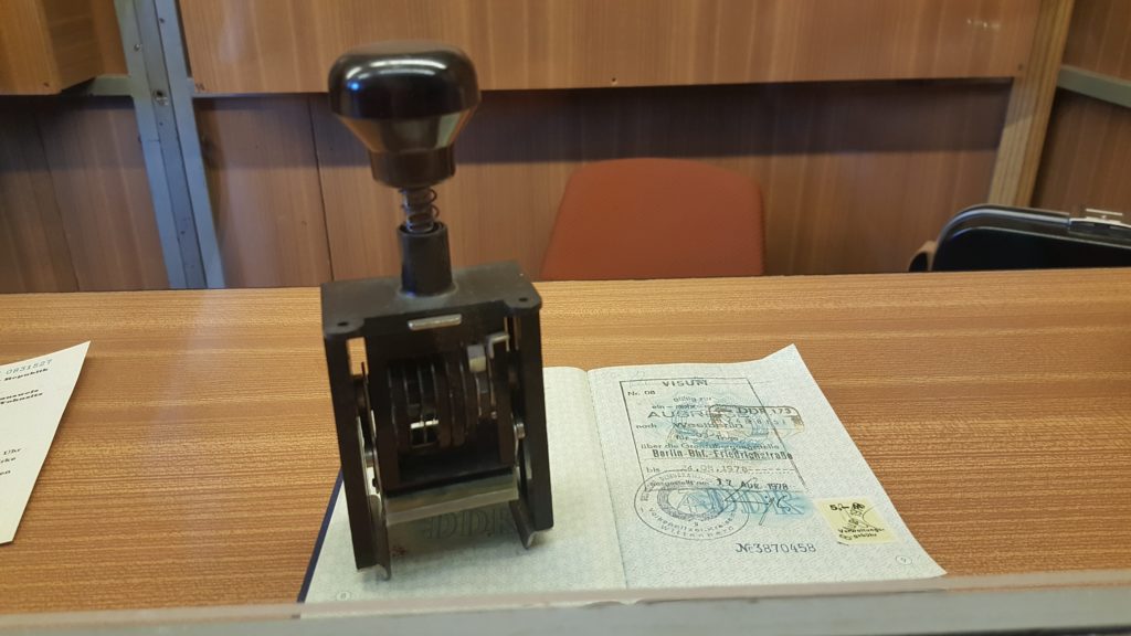 Blick auf den Tisch einer Kontrollkabine auf dem sich ein aufgeschlagener Pass und Stempel befinden.