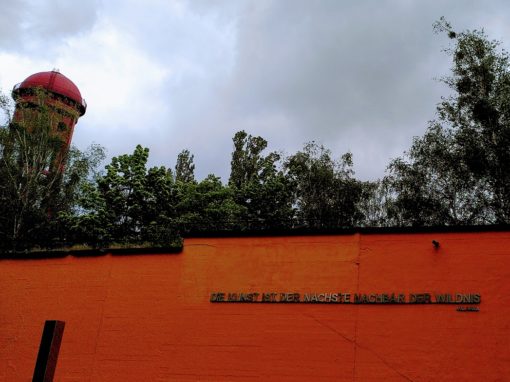 Eingangsbereich des Wasserturms mit orange-farbener Wand und einem Zitat zur Harmonie von Wildnis und Kunst in Metalllettern.