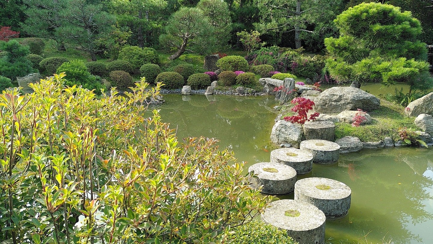 Teich mit runden Trittsteinen und am Ufer runde kleine Büsche und Nadelbäume.