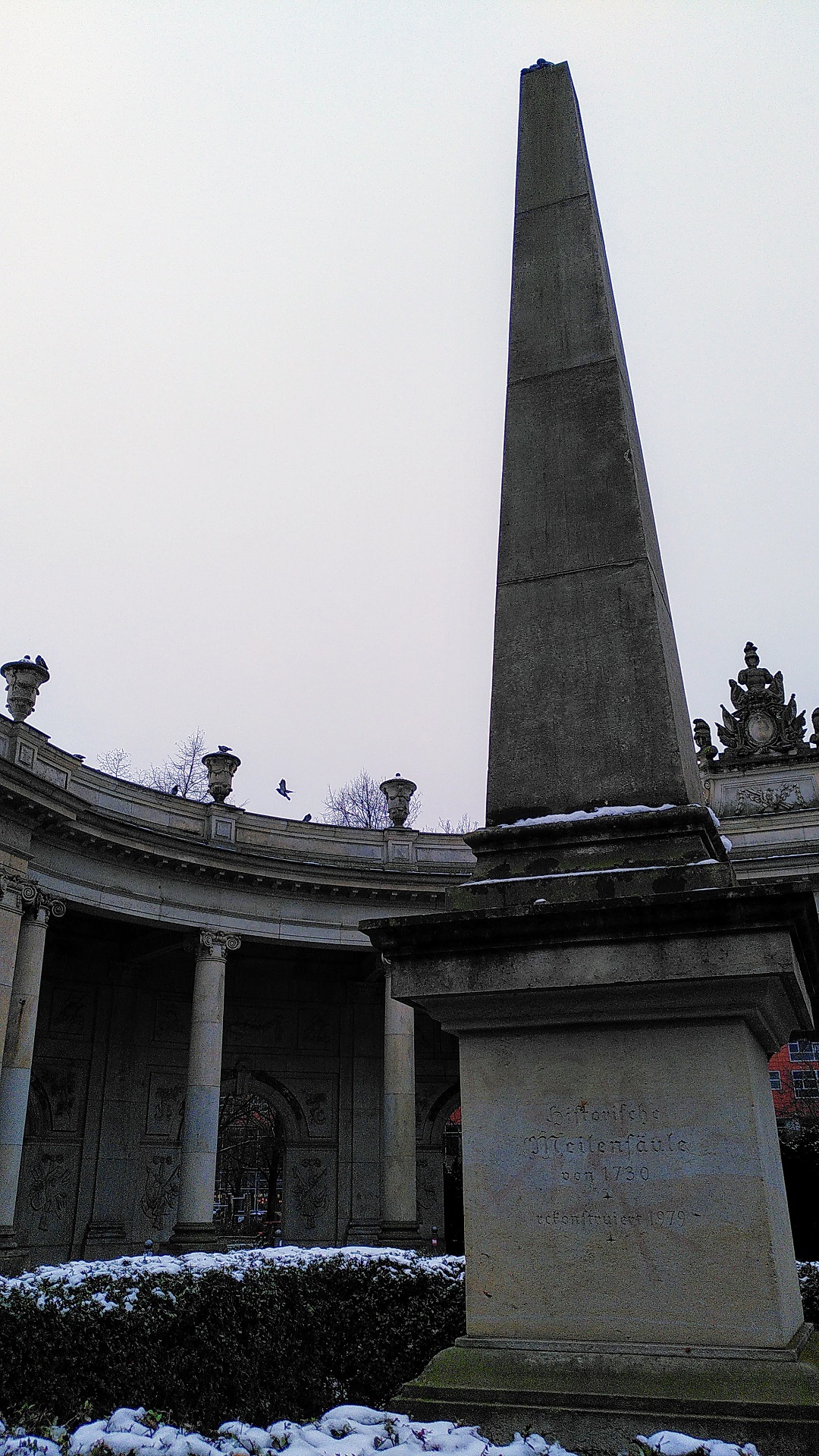Obelisk mit Kolonnaden im Hintergrund.