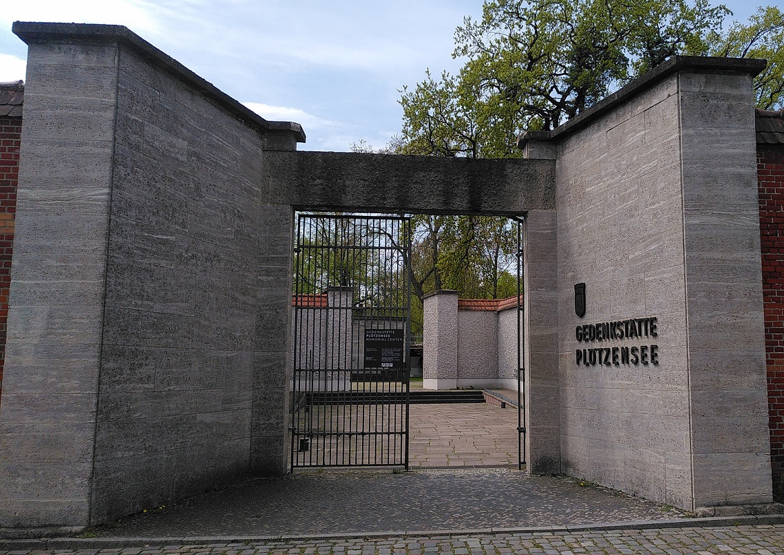 Eingangsbereich der Gedenkstätte Plötzensee: In einer Betonmauer öffnet sich ein vergittertes Stahltor zur Gedenkstätte hin.