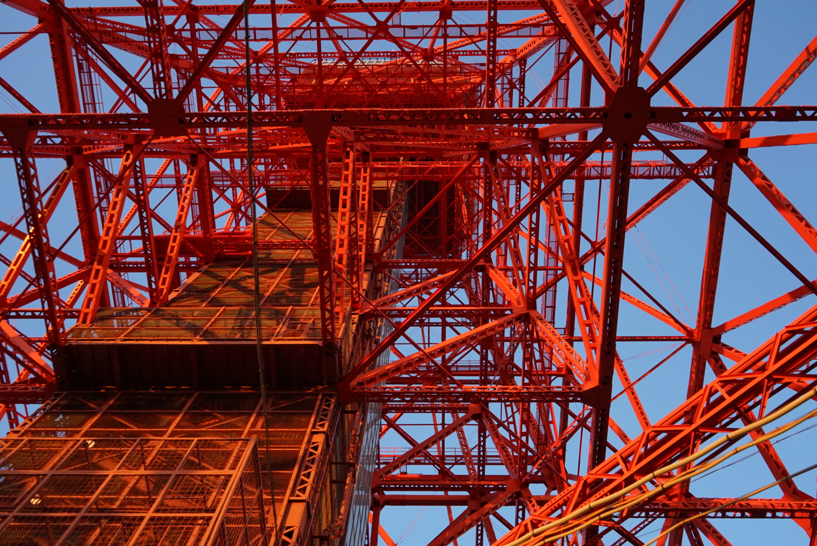 Blick auf die Konstruktion des Tokyo Tower von unten mit orangenen Stahlträgern und blauem Himmel.