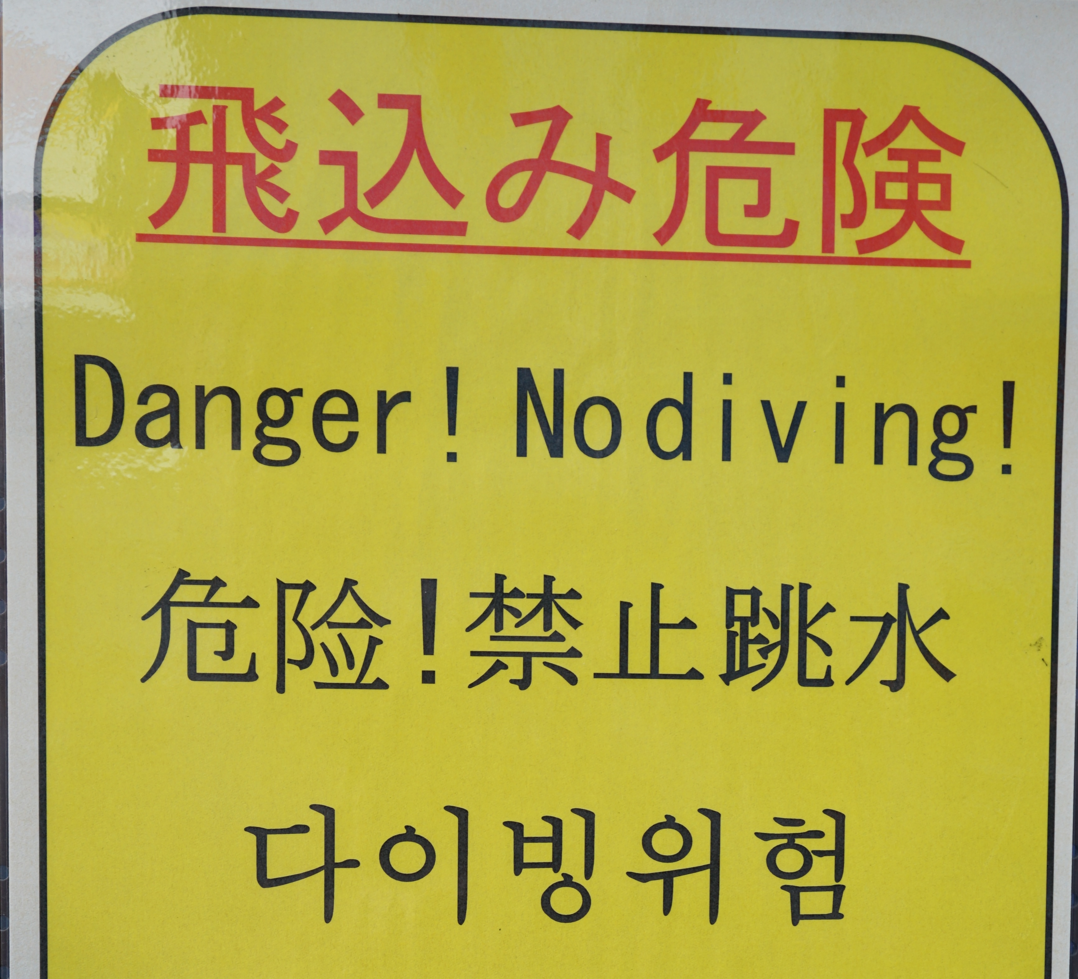 Gelbes Warnschild auf dem "Danger! No diving!" steht.