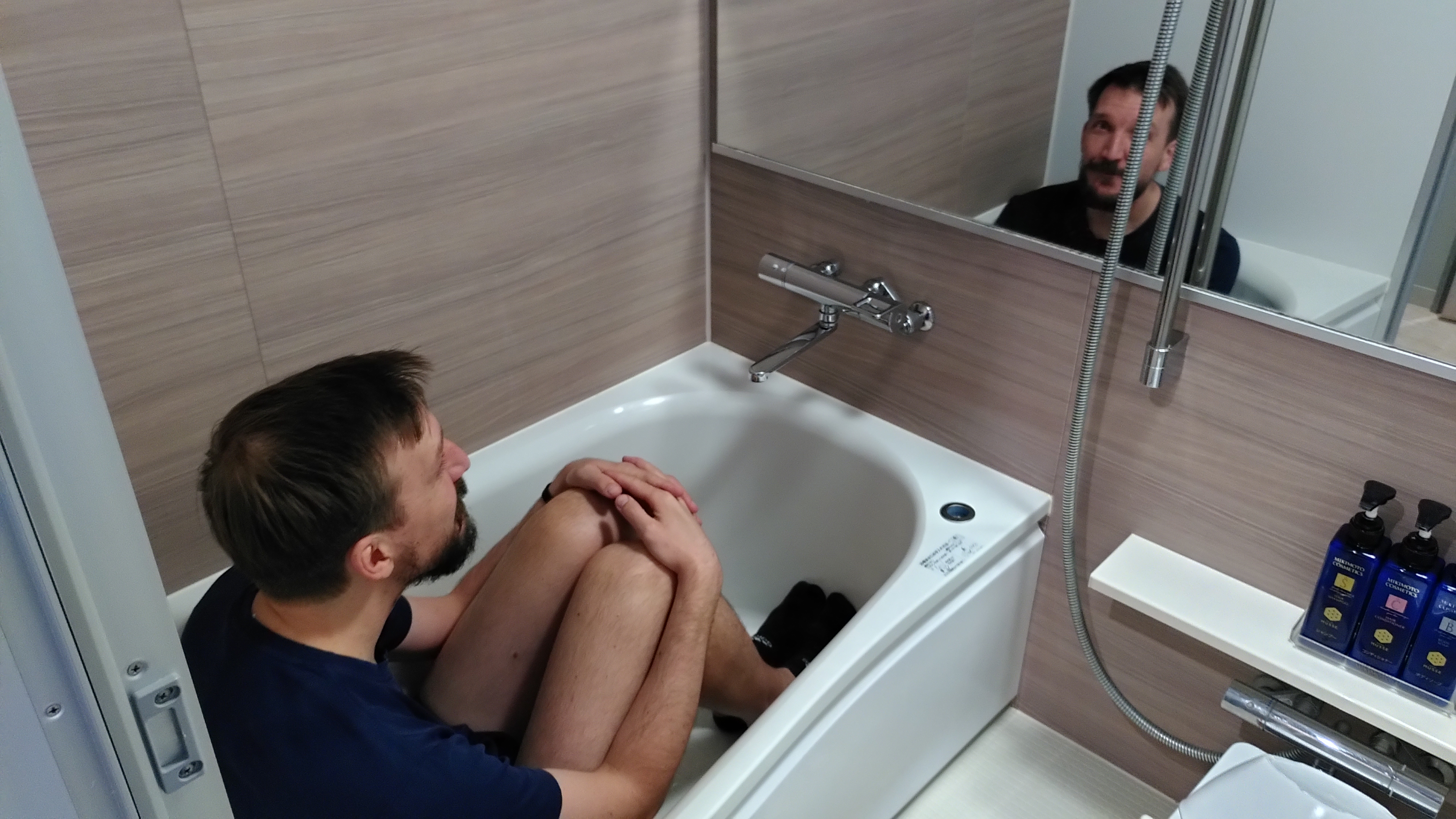 Ein Mann sitzt mit angezogenen Beinen in einer kleinen Badewanne.