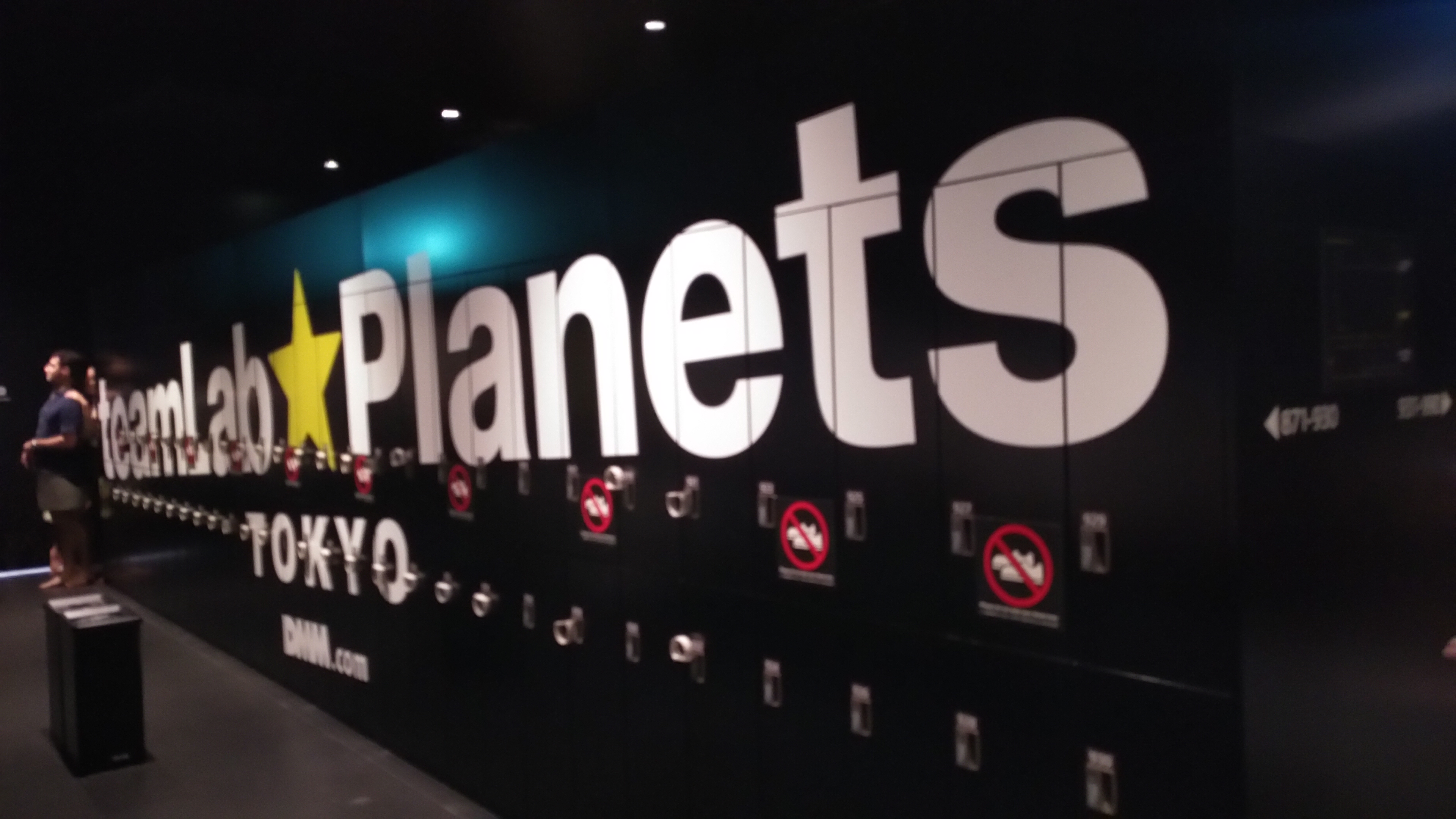 Blick auf schwarze Schließfächer, auf denen der Schriftzug teamLab Planets Tokyo zu lesen ist.
