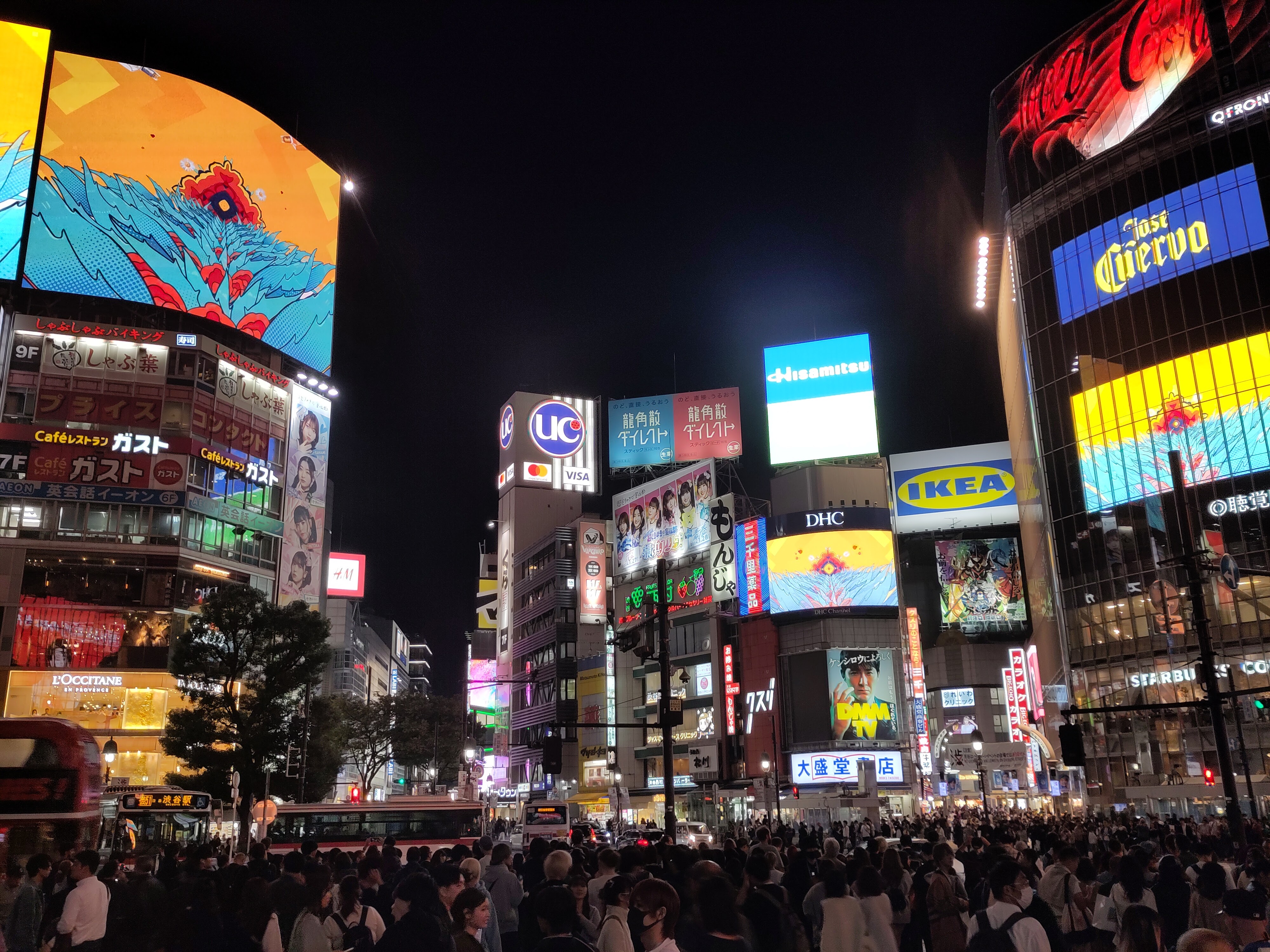 Blick auf die Shibuya-Kreuzung: Hochhäuser mit leuchtender Werbung und Menschenmassen.