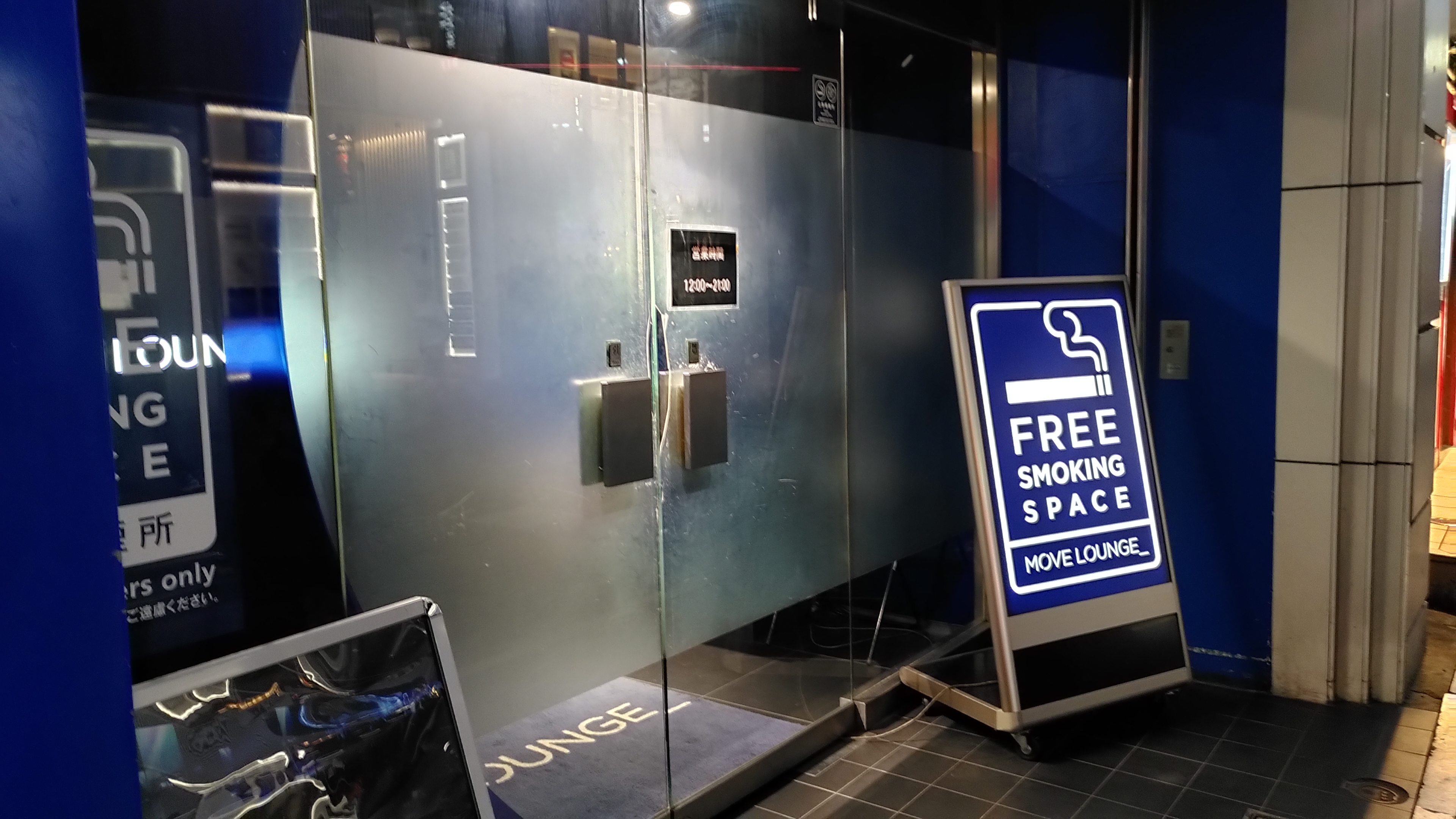 Blick auf eine Glastür vor der ein Schild mit der Aufschrift "Free Smoking Space" steht.