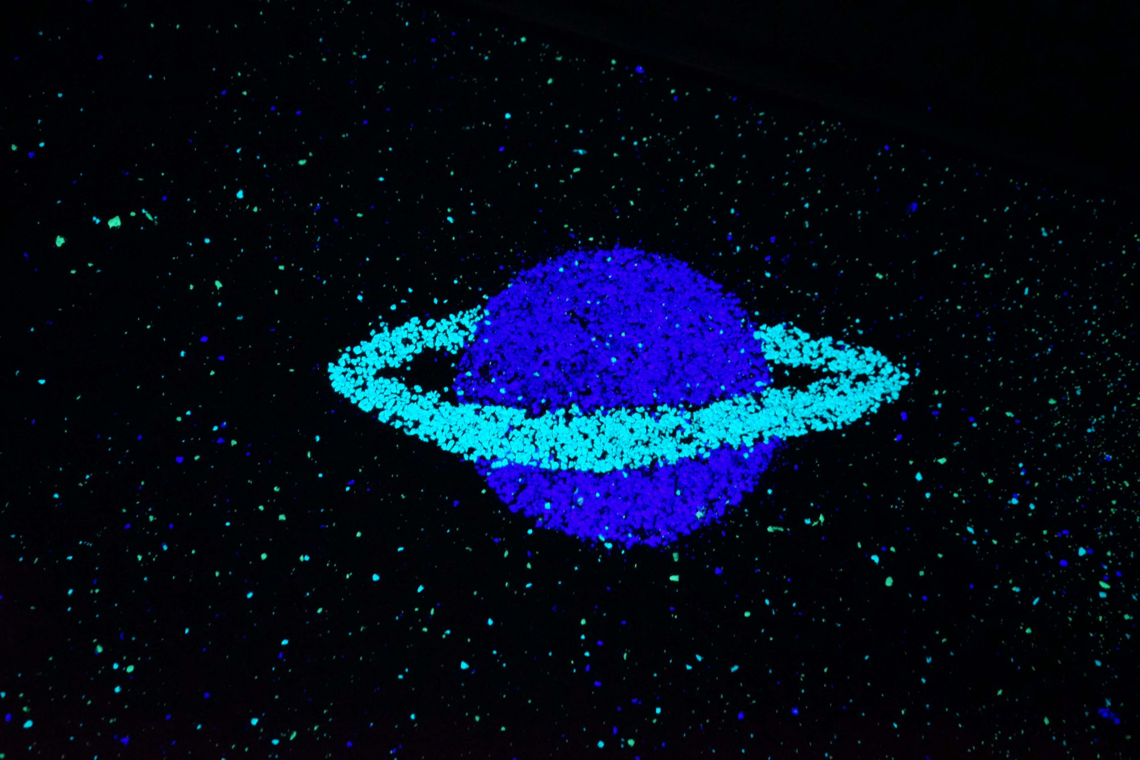 Blick auf den mit Schwarzlicht angeleuchteten Boden der Aussichtsplattform: grün-blau leuchtende Sprenkel und ein Planet mit Ring sind zu sehen.