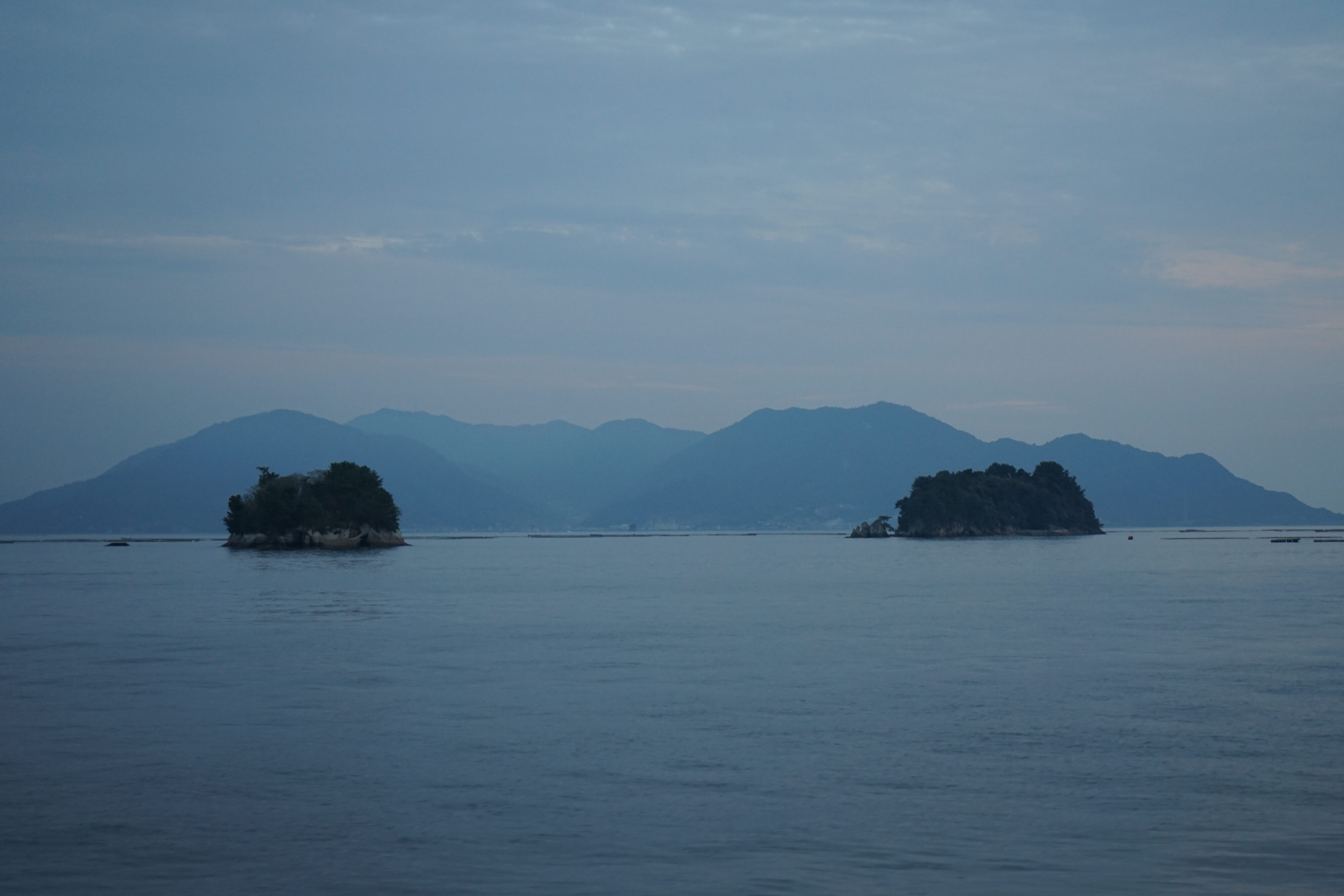 Blick auf das Meer mit zwei kleinen Inseln und im Hintergrund sind weitere größere Inseln mit Hügeln zu erkennen.