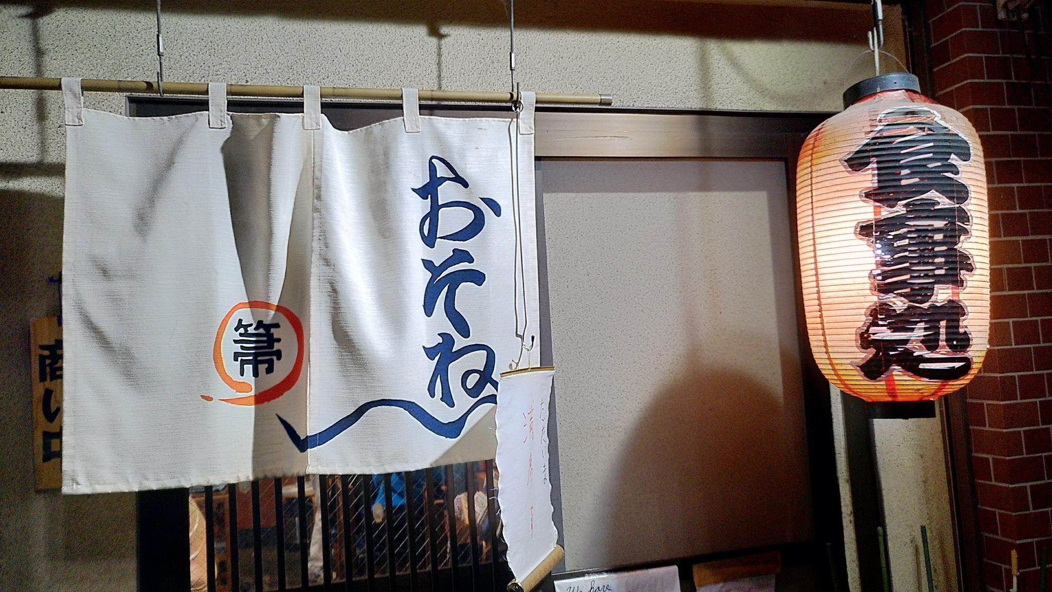 Eingangsbereich einer japanischen Kneipe mit roter Papierlampe und weißem Vorhang vor der Tür.