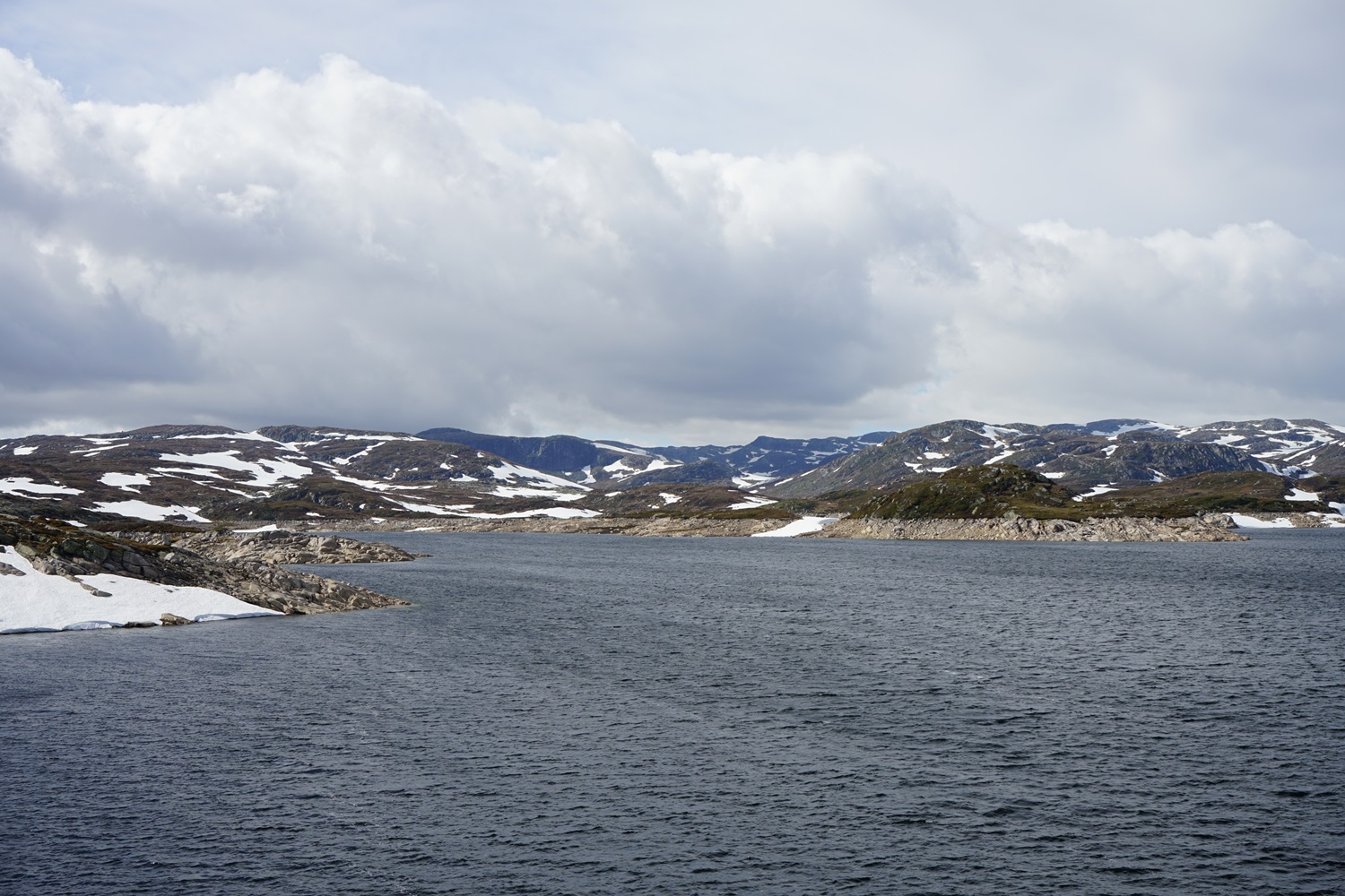 Blick auf einen See. Im Hintergrund schneebedeckte Hügel.