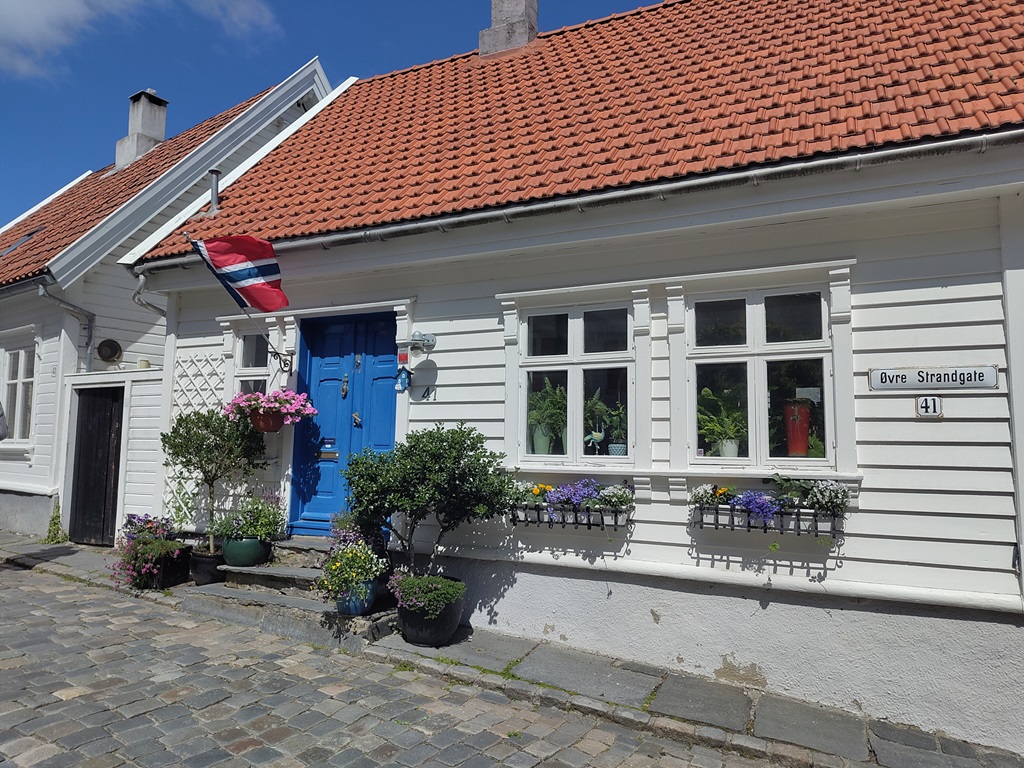 Weißes Holzhaus mit blauer Tür und Norwegenflagge.