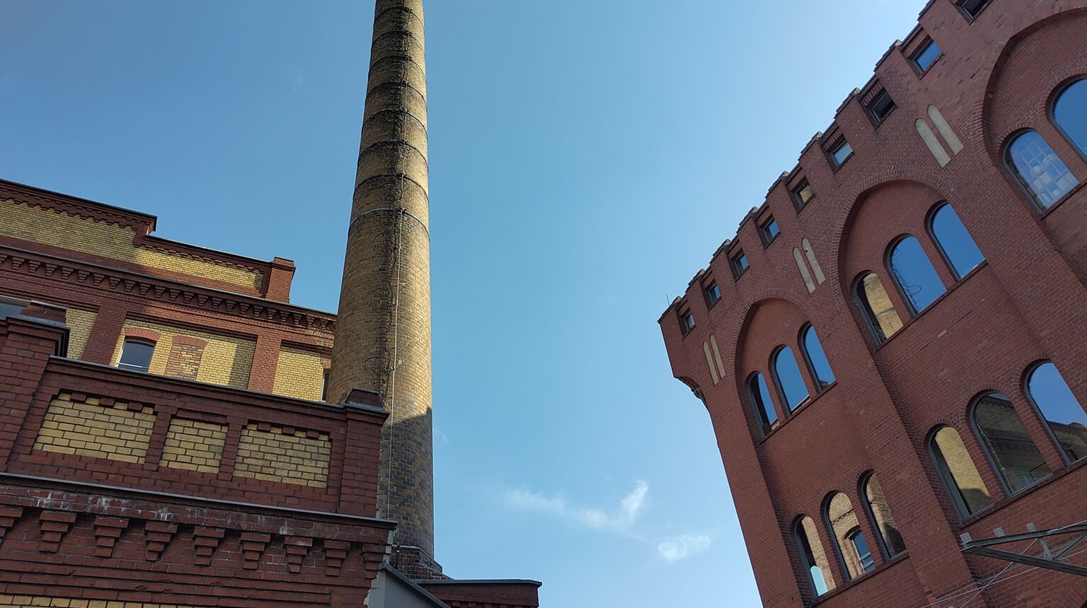 Backsteinbauten und ein Schornstein vor blauem Himmel.