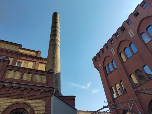 Backsteinbauten und ein Schornstein vor blauem Himmel.