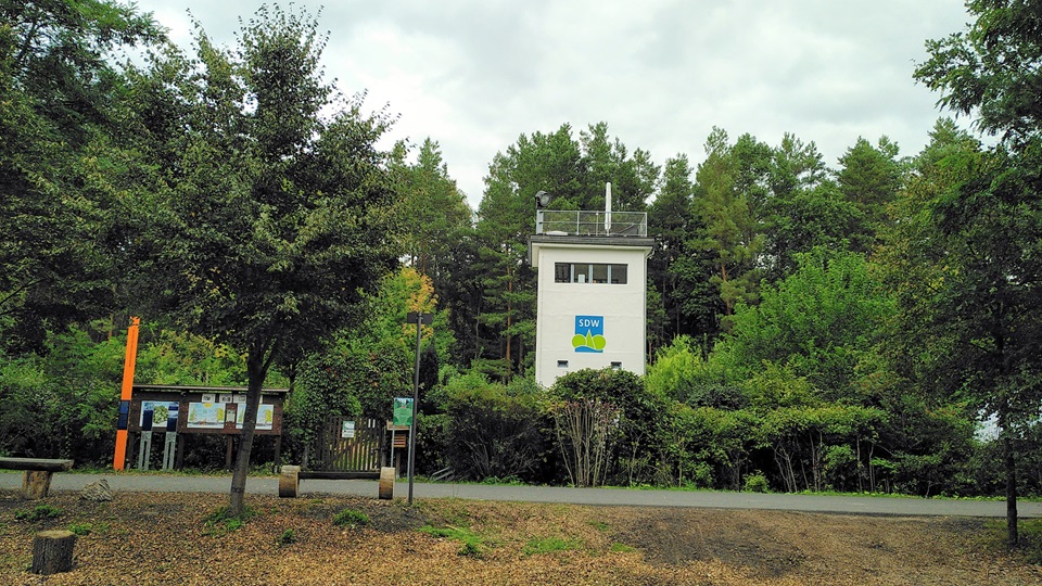 Ehemaliger Wachturm in Frohnau umgeben von Bäumen und Büschen, direkt daneben steht eine orangefarbene Stele.