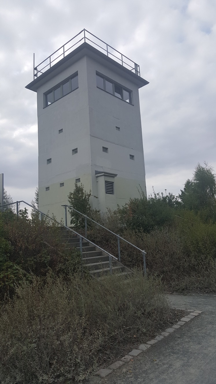 Eckiger Turm. Im Vordergrund eine Treppe und Büsche.