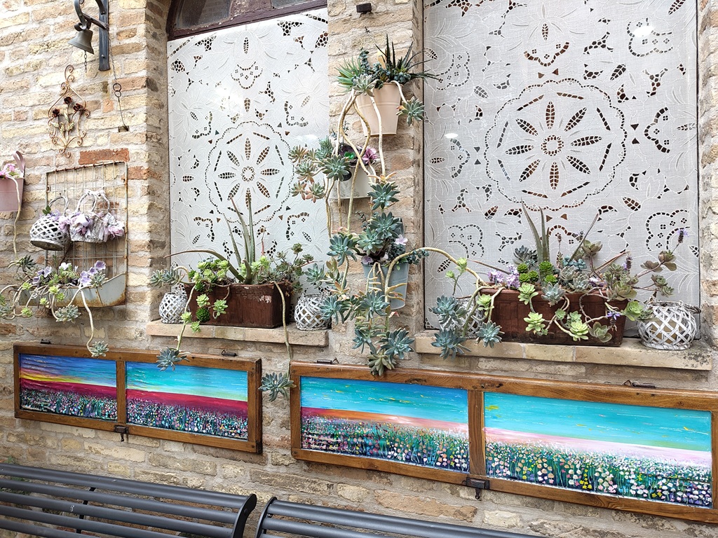 Fensterbrett voller Pflanzen und unter den Fenstern bunte Blumenbilder.
