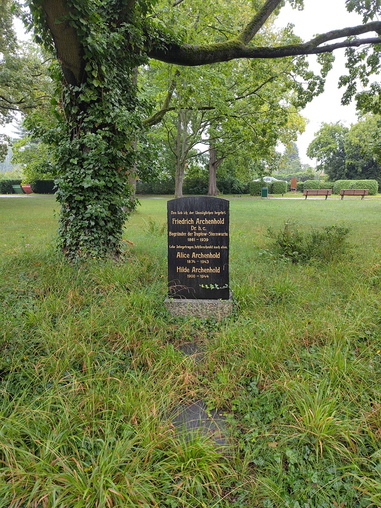 Schwarzer Familiengrabstein der Archenhold neben einem Baum auf einer wuchernden Wiese.