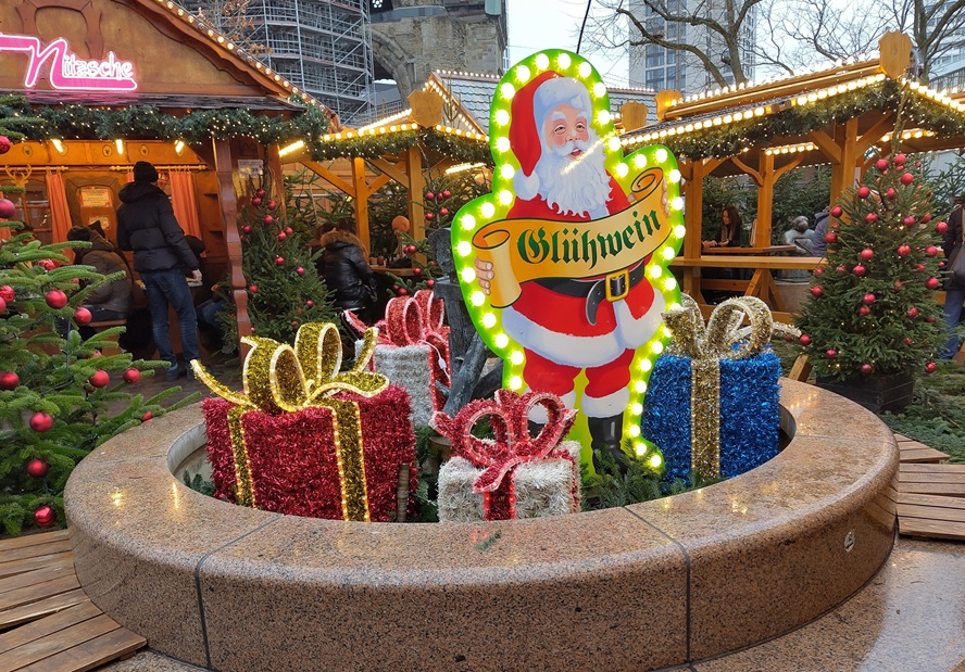 Pflanz-Rotunde, die mit leuchtenden Geschenken und einer Weihnachtsmannfigur mit einem Glühweinschild gefüllt ist.