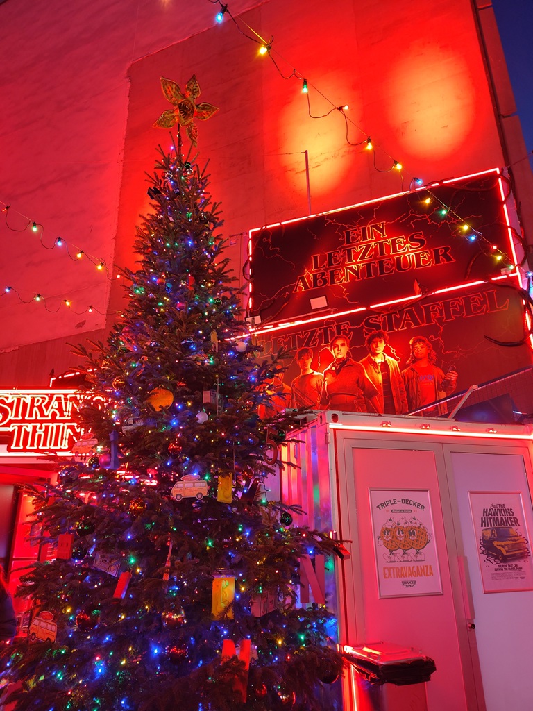 Weihnachtsbaum mit Dekoration, die Bezug zur Serie Stranger Things hat und im Hintergrund Gebäudewand mit Postern zur neuen Staffel.
