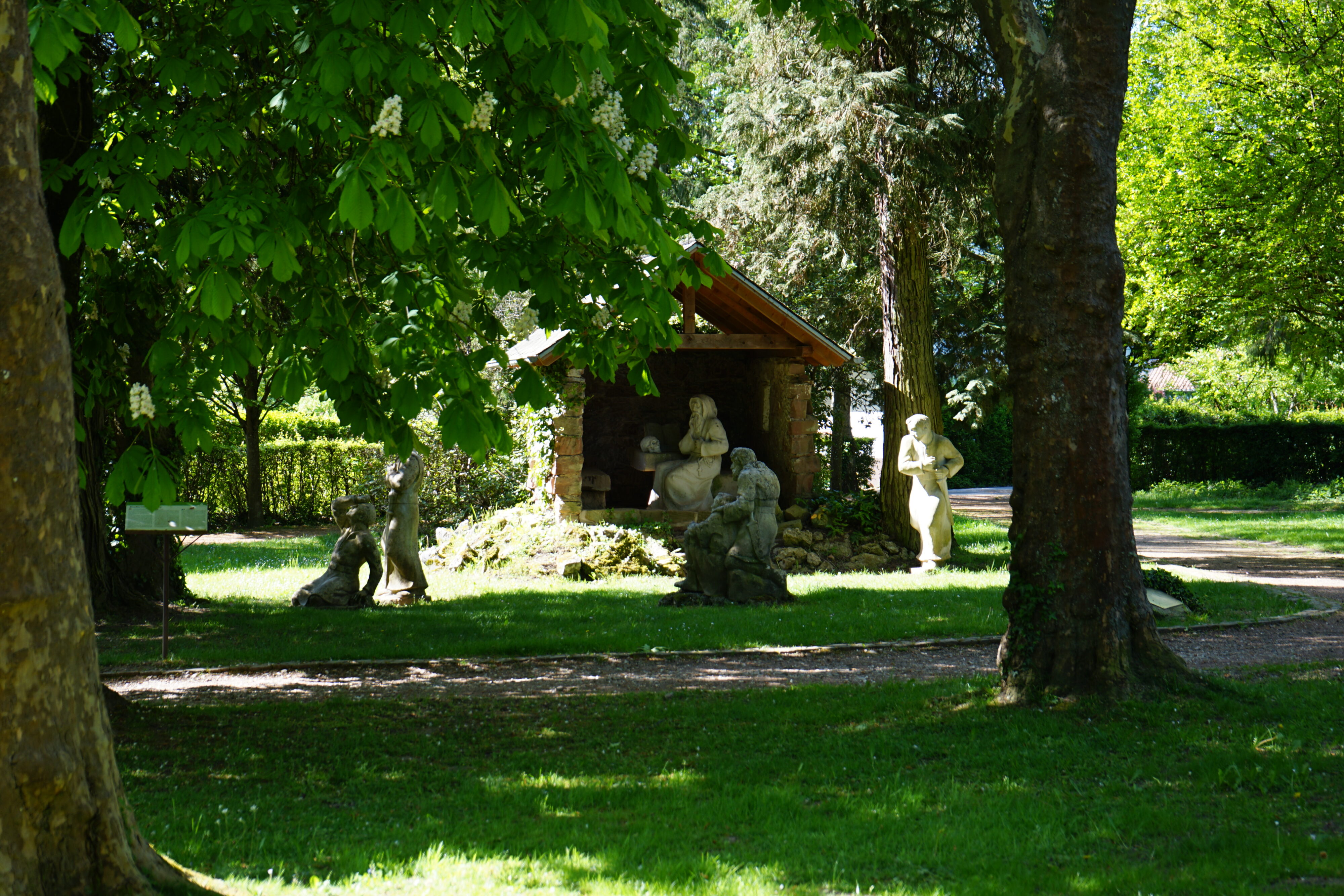 Steinfigurenensemble auf einem Rasen umgeben von Bäumen.