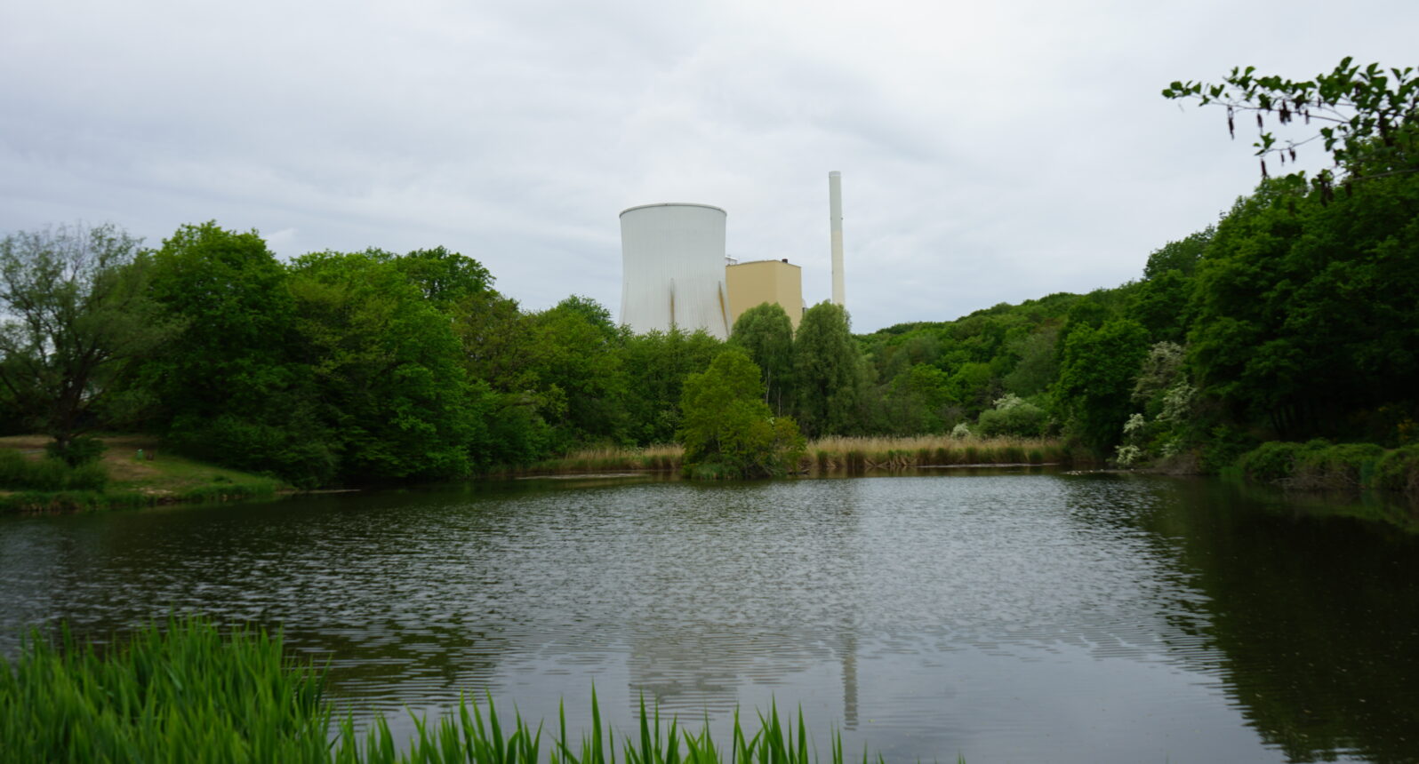 Blick auf einen Weiher und im Hintergrund ein Kraftwerk mit zwei Türmen.